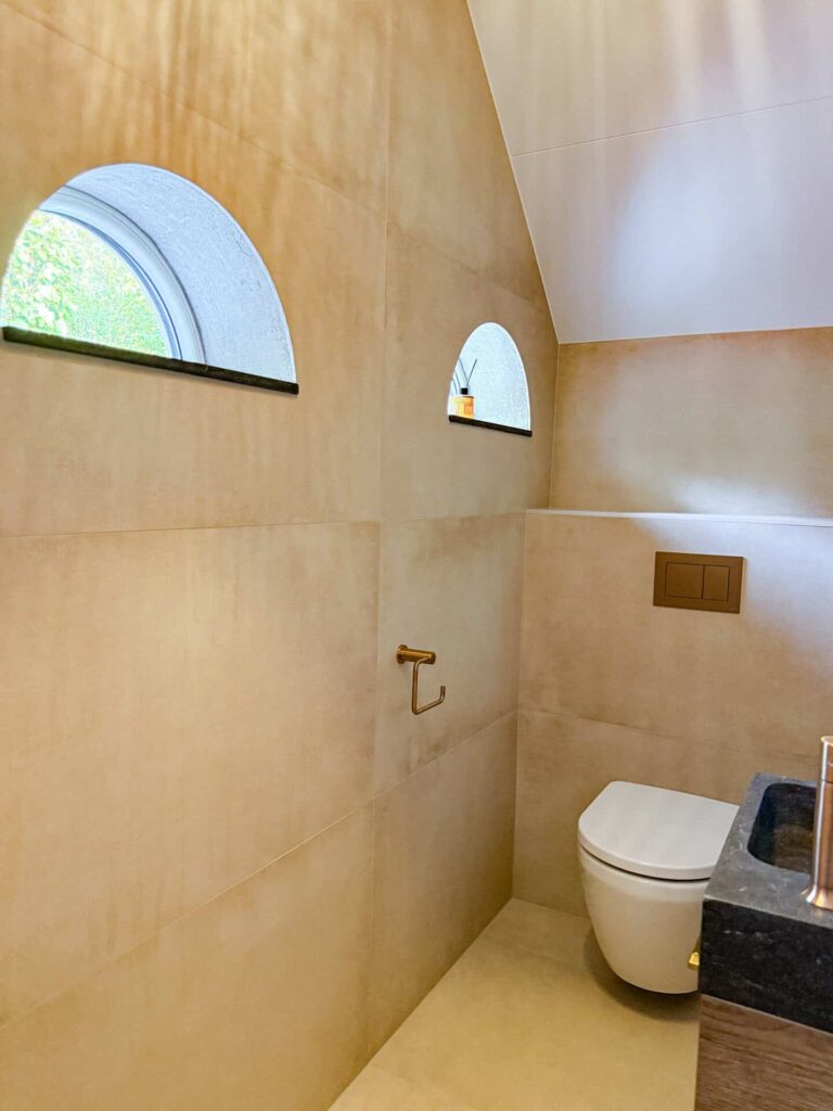 Toilet met ronde boerderijramen en beige tegelwerk